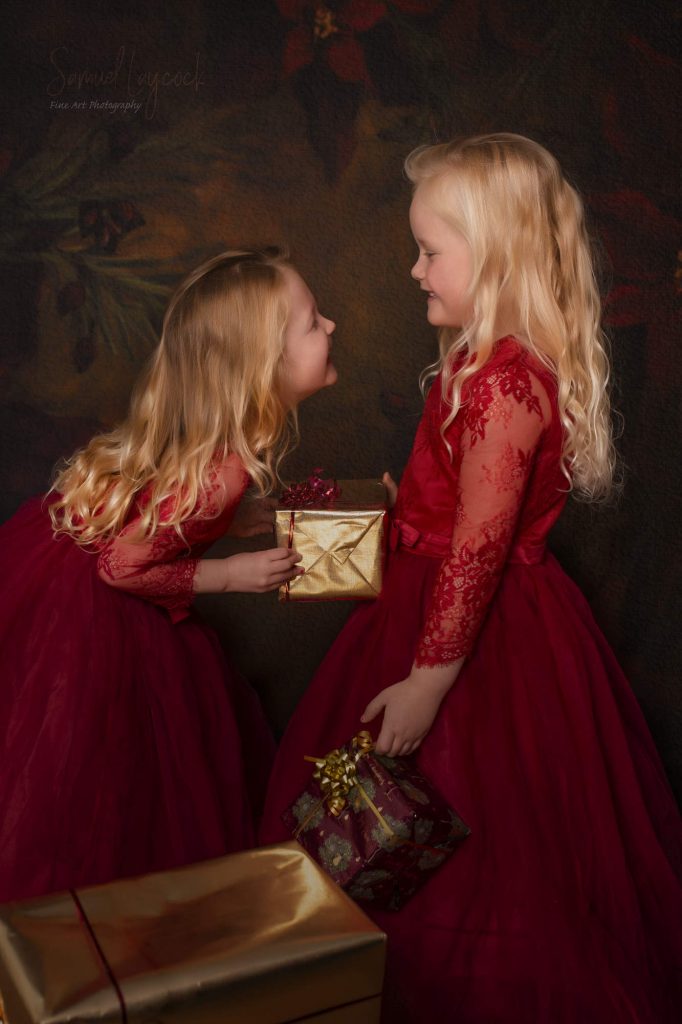 Two young girls wearing red dresses enjoying a moment with a present