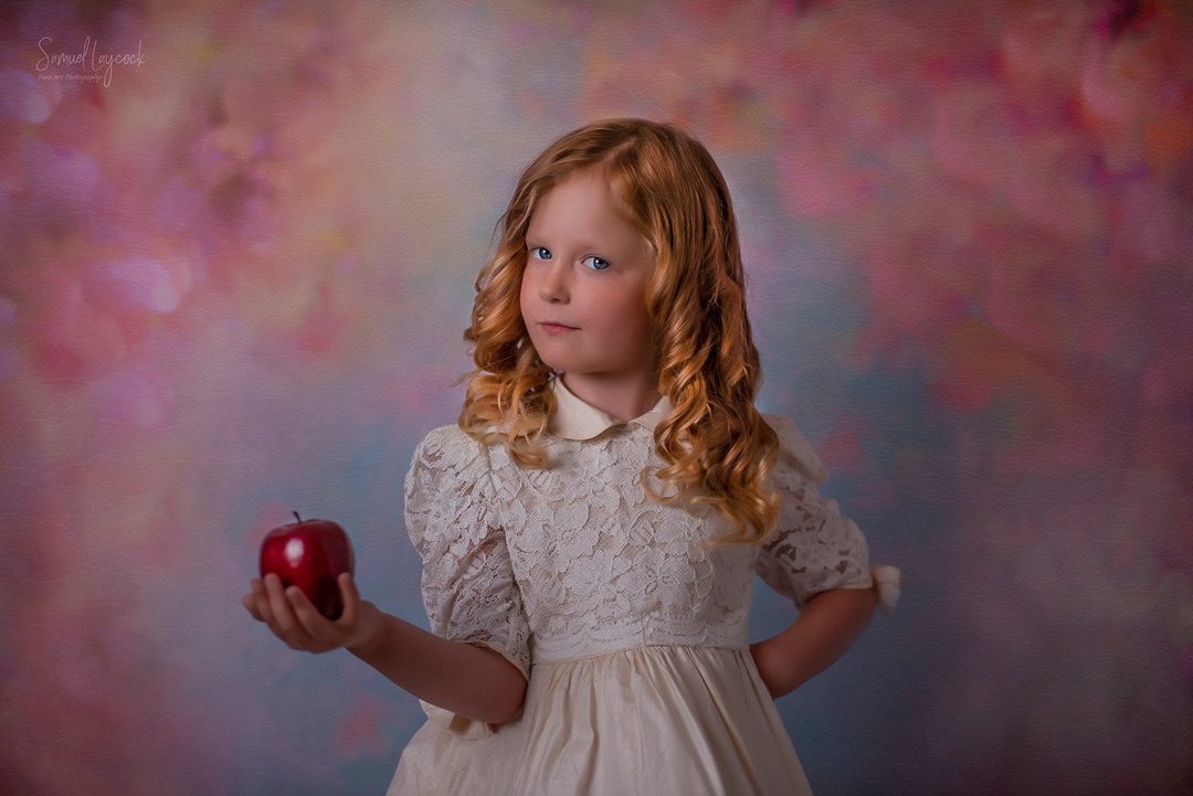 Young girl with hand on hop holding an apple in the other hand.