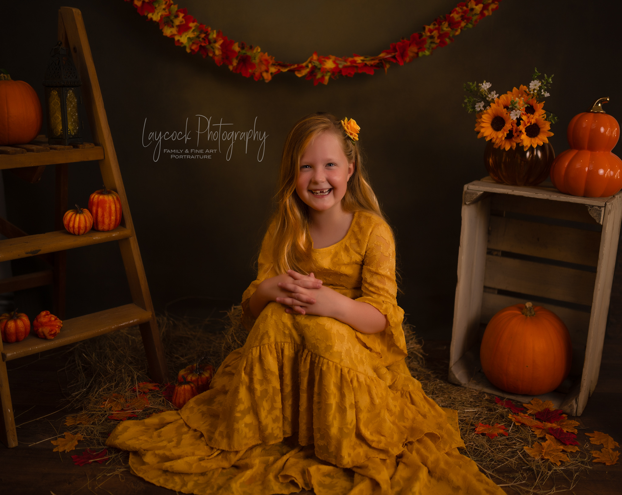 Young girl sat on straw with aumnal leaves and pumpkins around her