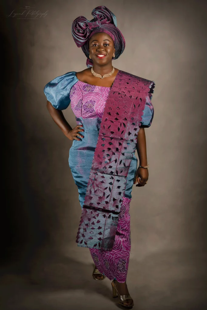 African woman wearing traditional dress. Stood upright with her right hand on her hip facing forward.